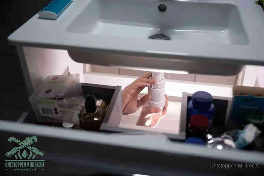 Een pompfles met zeep boven een wastafel, de heet water en afwasmiddel-methode om een vetprop in de afvoer los te maken in Mijdrecht