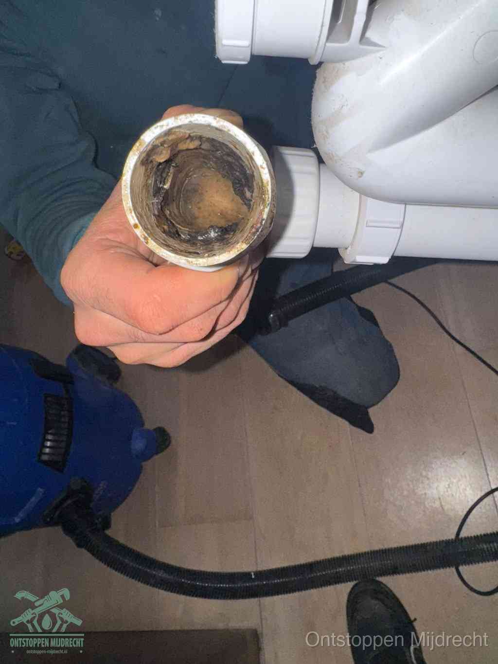 Een hand houdt een losgekoppeld PVC-afvoerbuisstuk vast dat van binnen volledig is dichtgeslibd met vet, vuil en aanslag, de meest voorkomende oorzaak van een verstopte afvoer in Mijdrecht