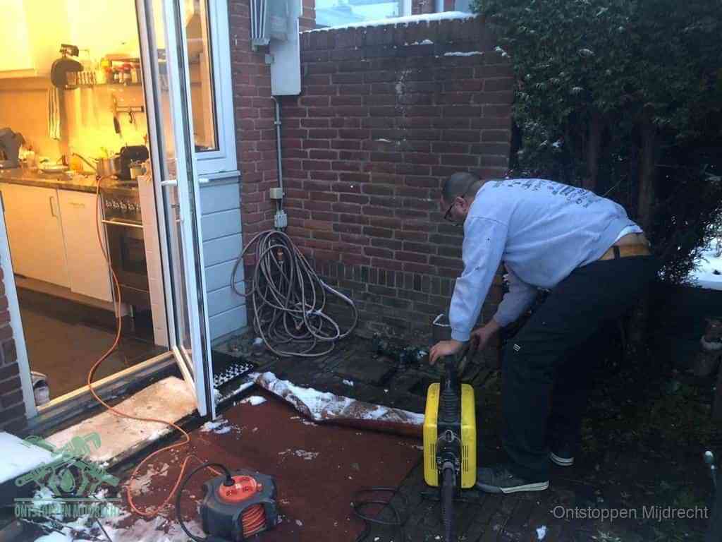 Een monteur werkt buiten bij een open riool-/grondput met een elektrische ontstoppingsmachine om een verborgen afvoerprobleem op te sporen in Mijdrecht