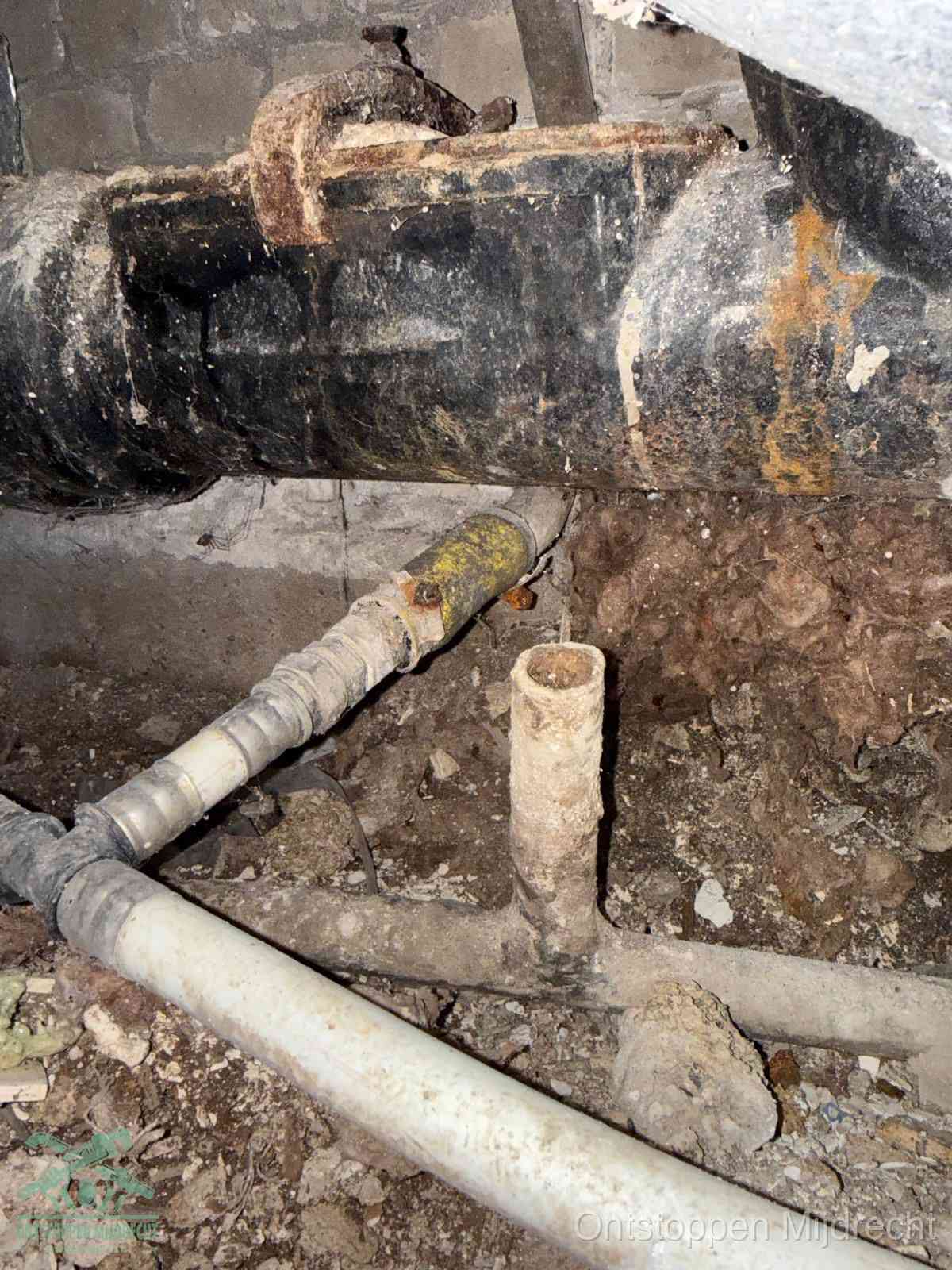 Een dikke zwarte hoofdrioolbuis met roest- en kalkaanslag in een kruipruimte, oorzaak van terugkerende structurele afvoerproblemen in Mijdrecht