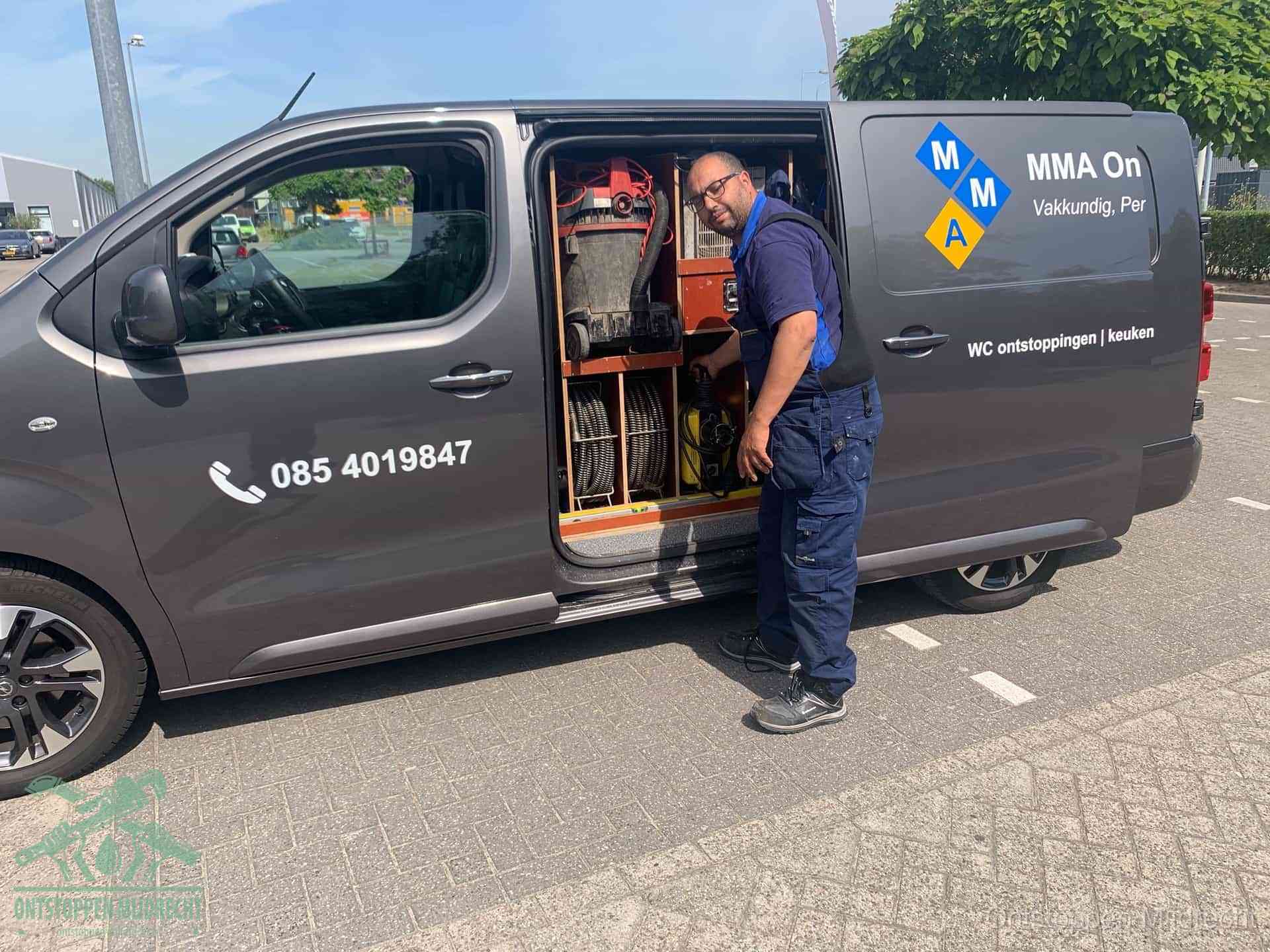 Een monteur bij de open schuifdeur van zijn bedrijfsbus op een parkeerplaats, klaar om de oorzaak van terugkerende afvoerverstoppingen aan te pakken in Mijdrecht
