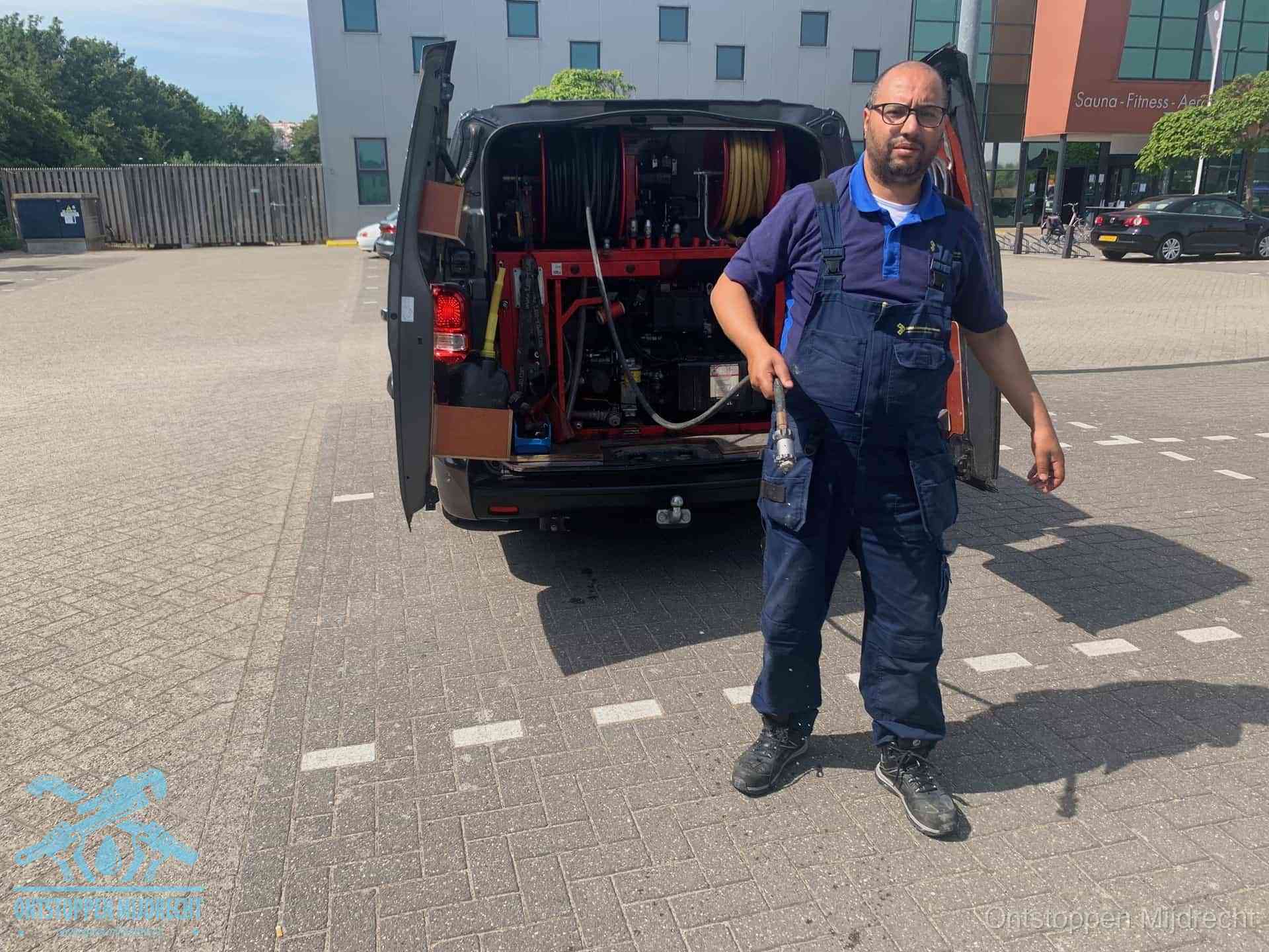 Een monteur bij zijn bestelbus met een hogedruk- en rioolreinigingsunit, klaar om de oorzaak van terugkerende wc-verstoppingen aan te pakken in Mijdrecht