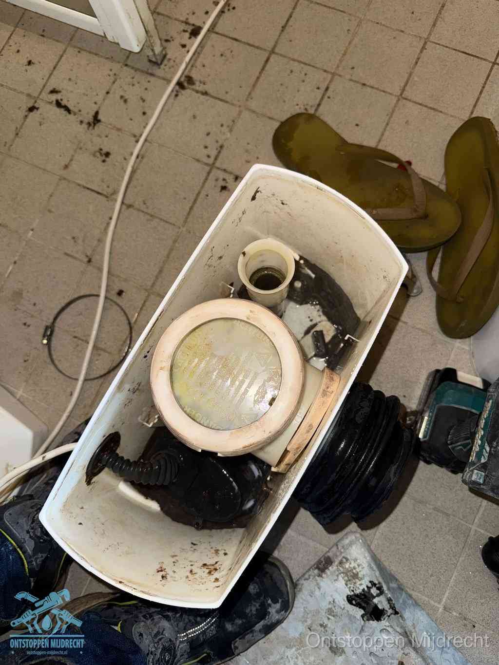 Een gedemonteerde toiletpot op de vloer met ontstoppingsveer en gereedschap ernaast, het verwijderen van een vastzittend voorwerp uit de wc in Mijdrecht
