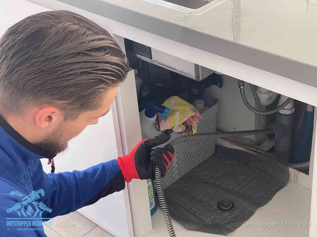 Een monteur voert een flexibele ontstoppingsveer in de afvoer om een verstopping voorbij de bocht van het toilet te bereiken in Mijdrecht