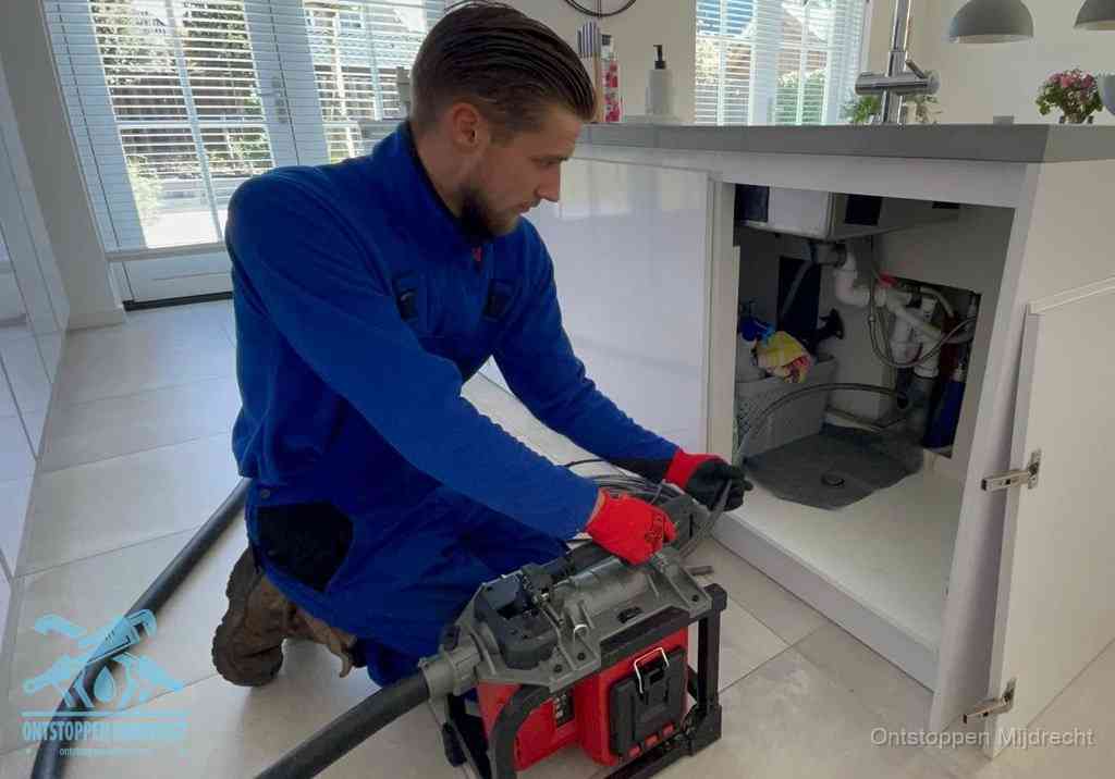 Werkwijze gootsteen ontstoppen in Mijdrecht Een monteur voert een professionele elektrische ontstoppingsmachine in de afvoer onder de spoelbak tijdens het gootsteen ontstoppen in Mijdrecht